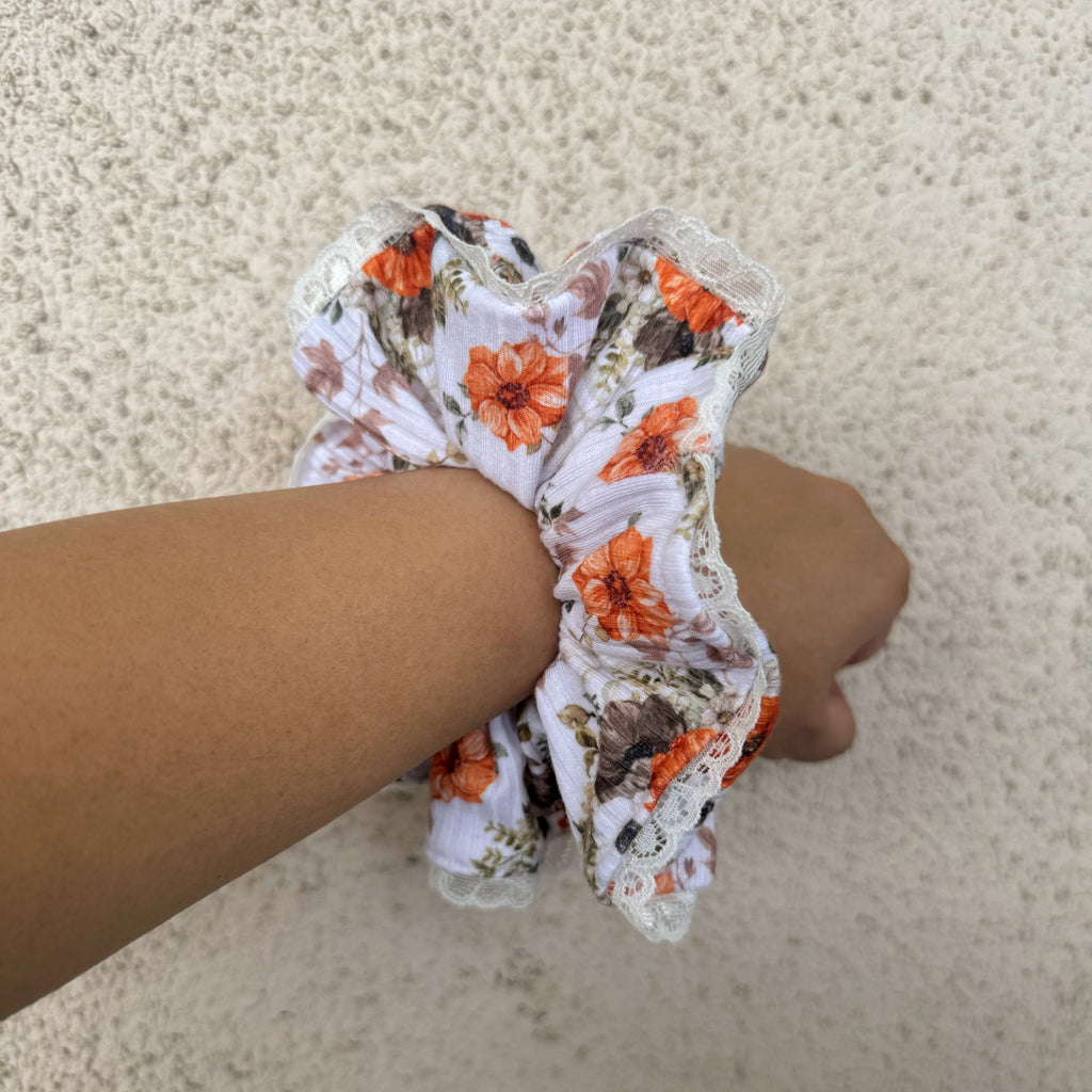 Floral scrunchie held by a hand on a beige carpet background