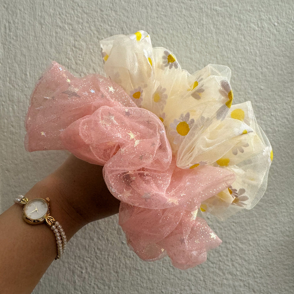 Hand holding pink and yellow scrunchies against a plain background