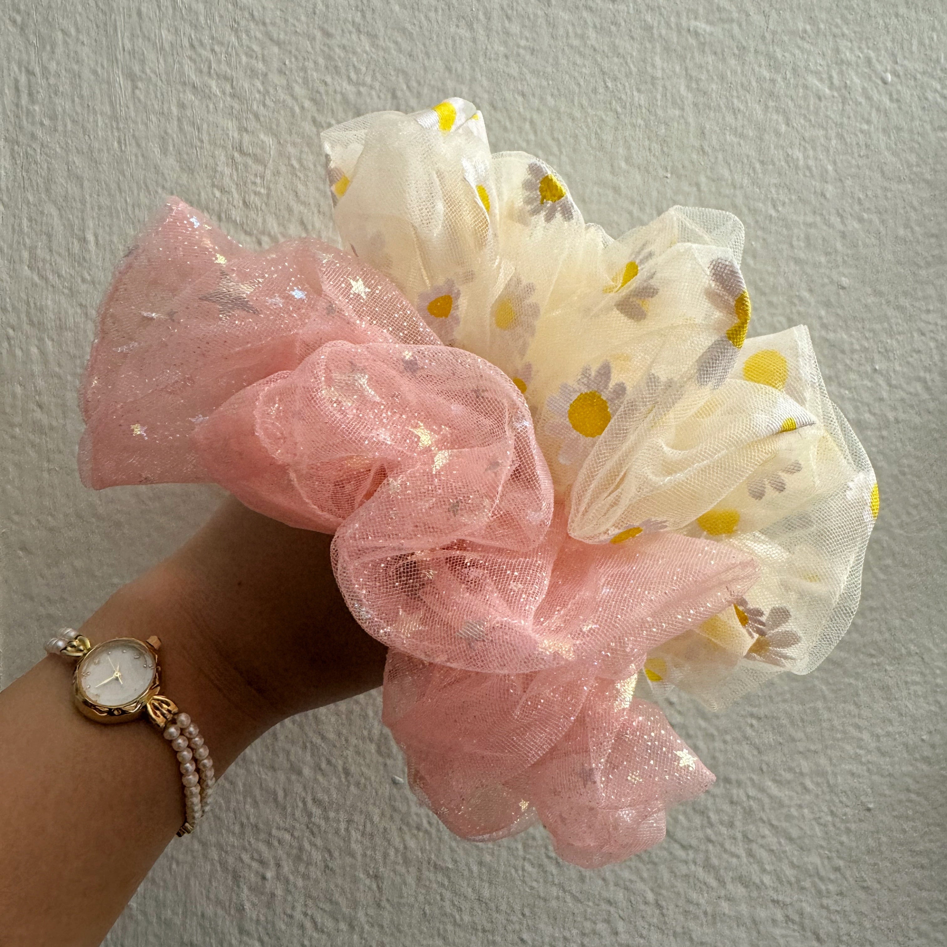 Hand holding pink and yellow scrunchies against a plain background