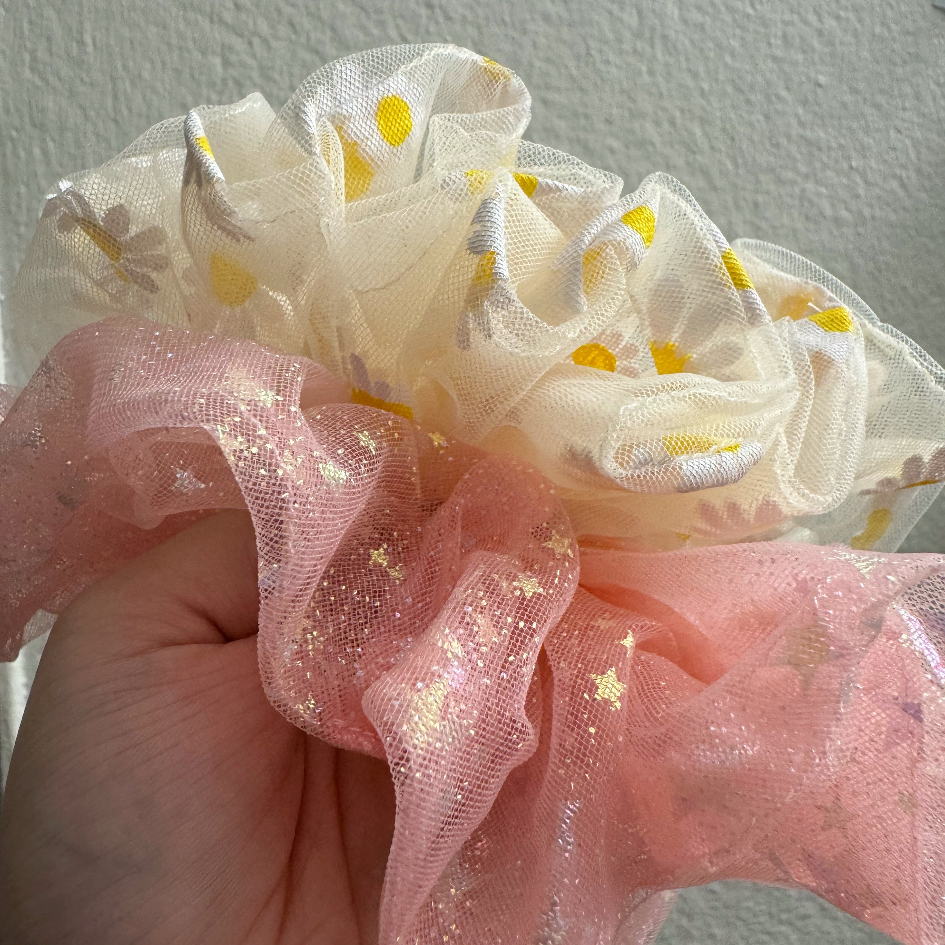 Pink and white floral scrunchie held by a hand against a neutral background
