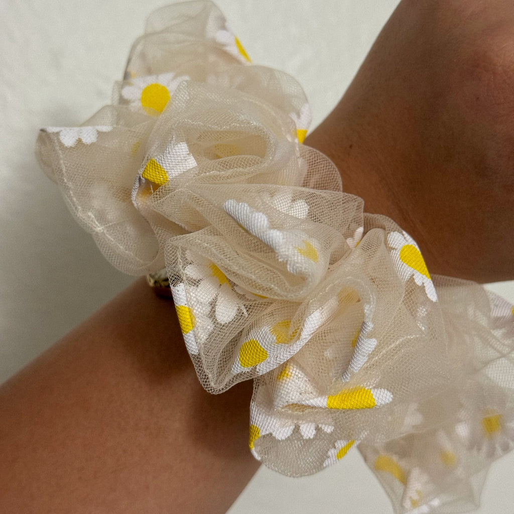 Beige scrunchie with floral pattern on wrist against a neutral background