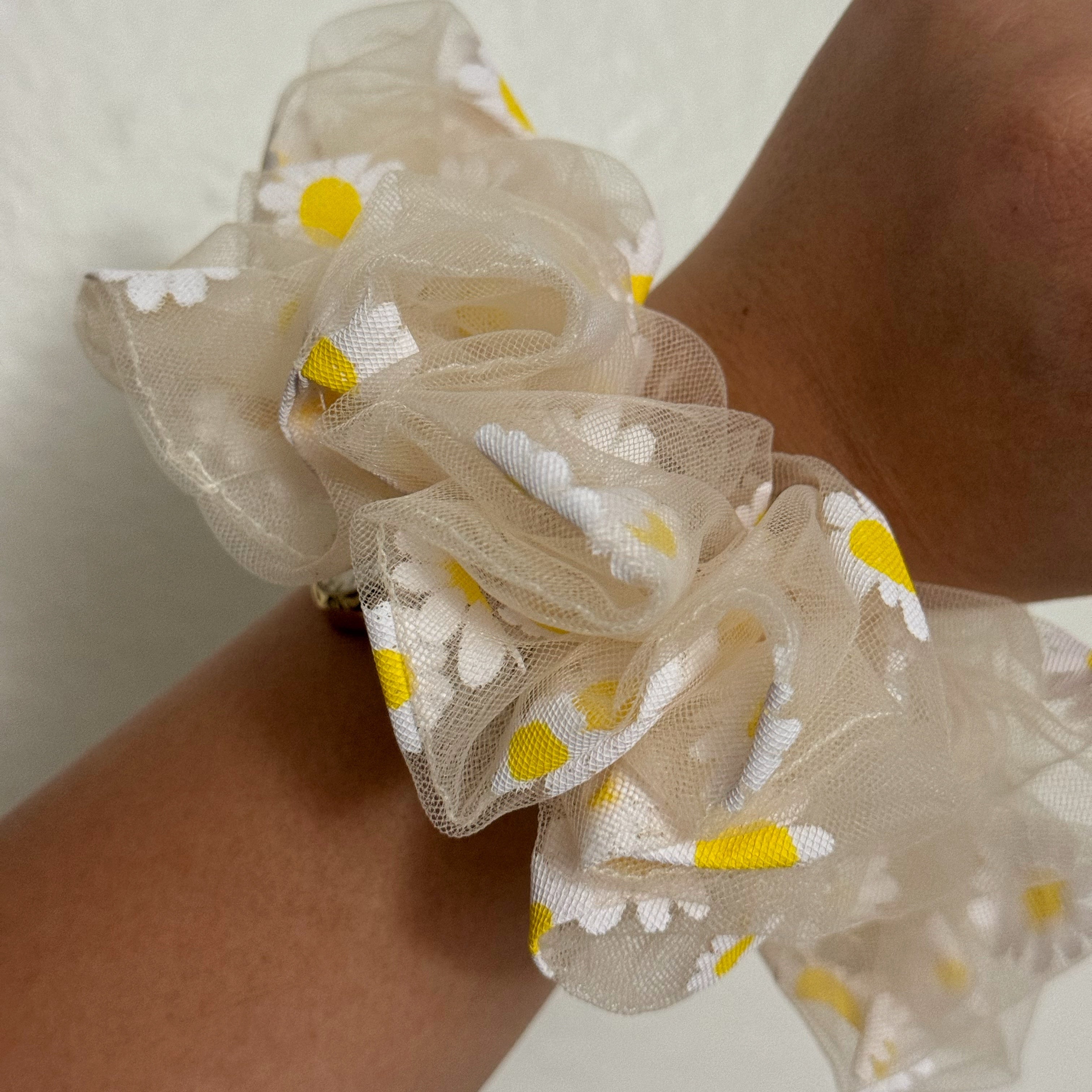 Beige scrunchie with floral pattern on wrist against a neutral background