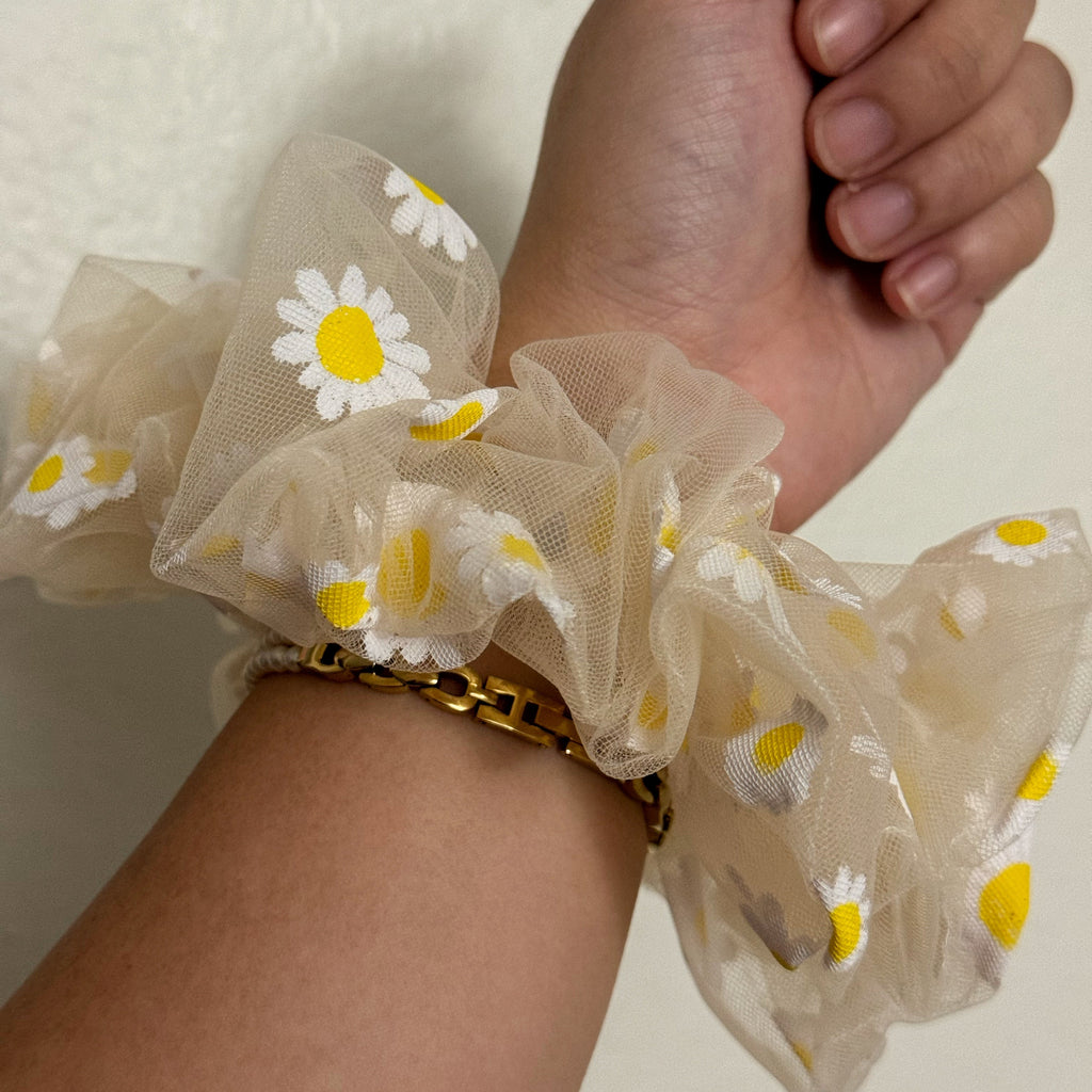 Hand wearing sheer scrunchie with daisy pattern on a plain background