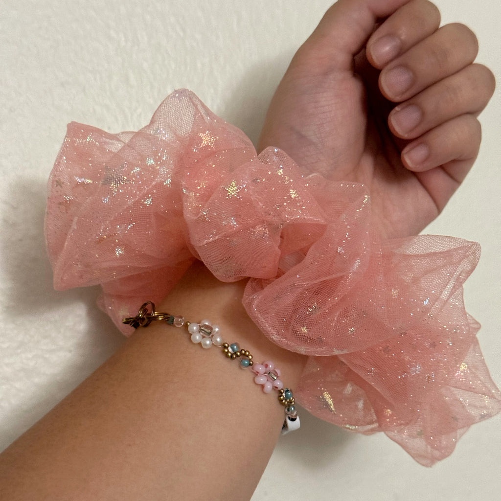 Hand wearing a pink scrunchie with a white background