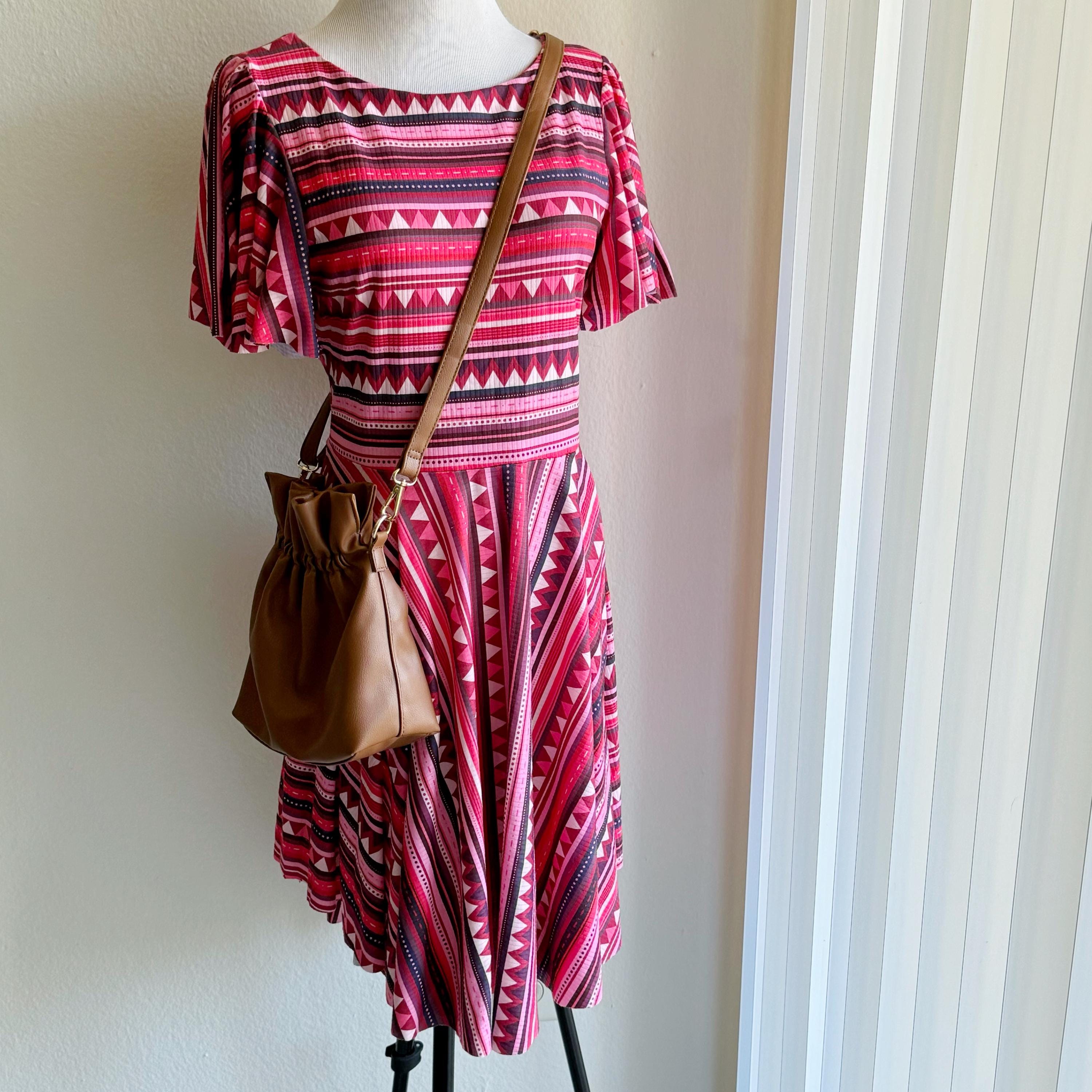 Mannequin wearing a red and black patterned dress with a brown bag against a white wall.