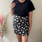 Person wearing a black t-shirt and floral skirt against a neutral background