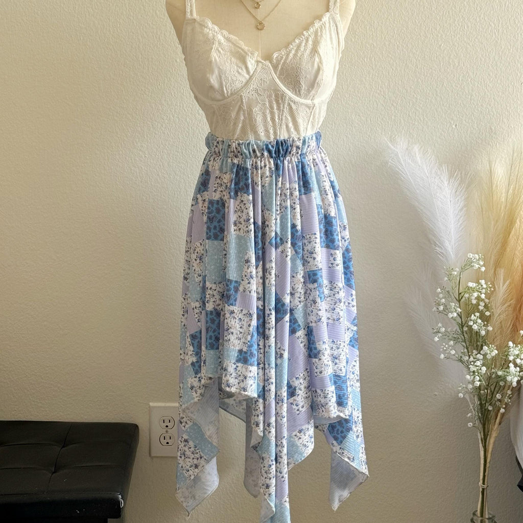 White lace top with a blue floral skirt on a mannequin against a neutral wall.