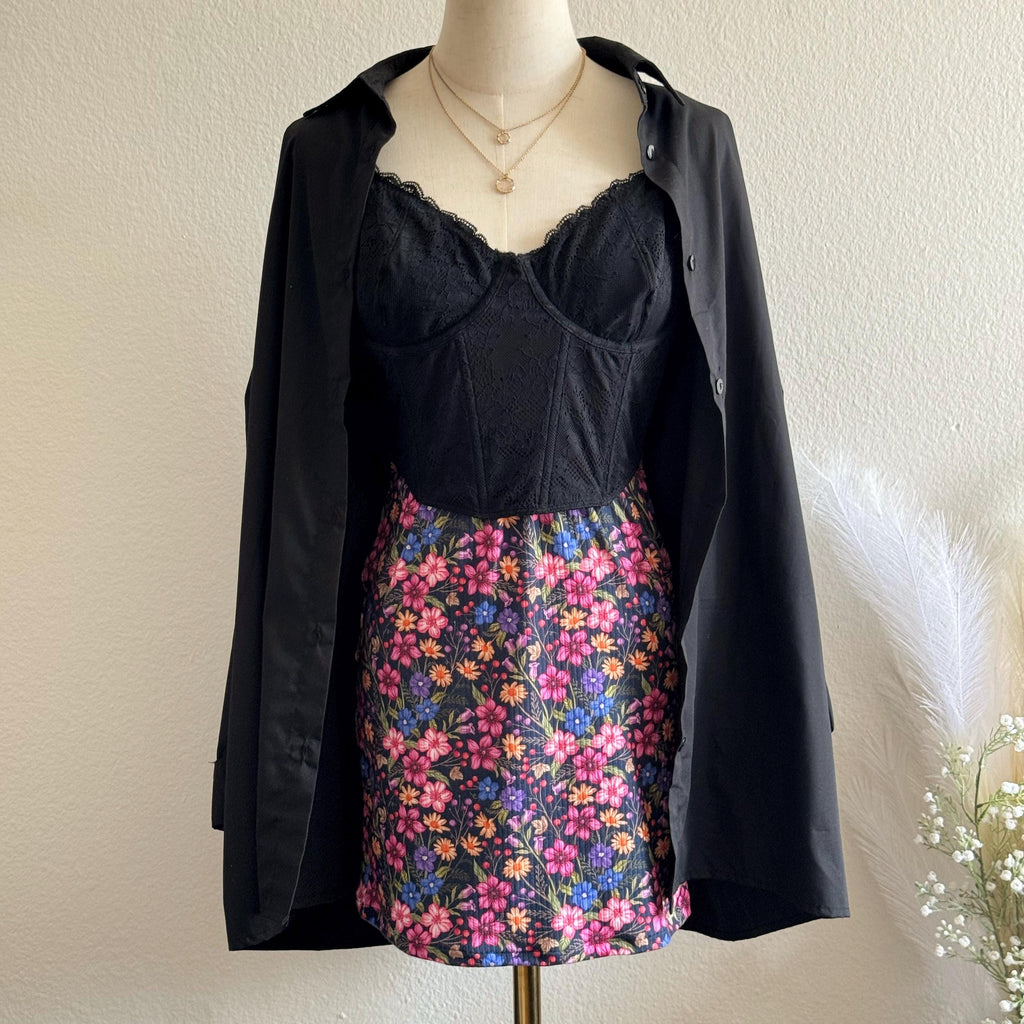 Mannequin wearing a black top and floral skirt with a dark coat over it, against a plain background.