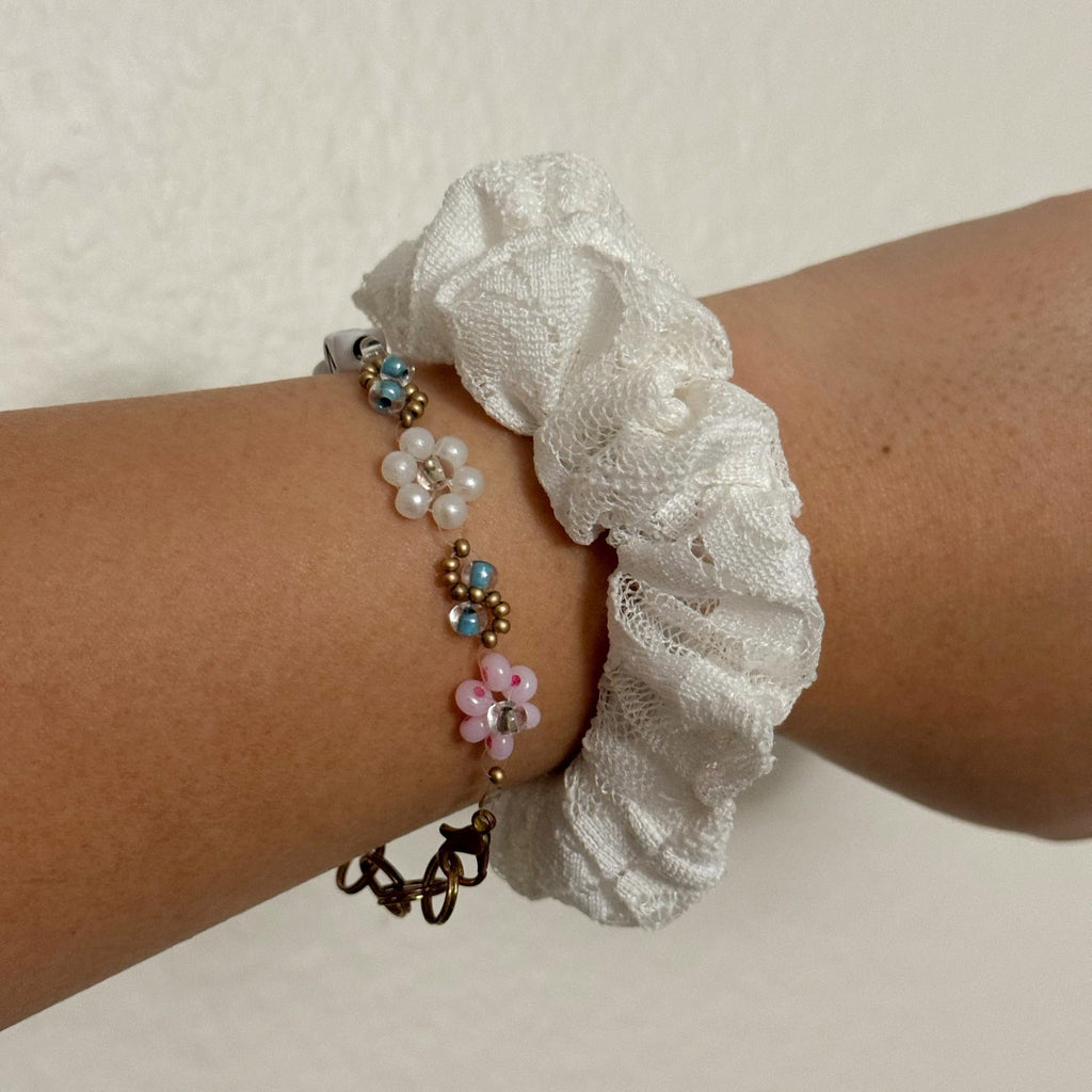 Wrist with a white lace scrunchie and colorful beaded bracelet on a light background