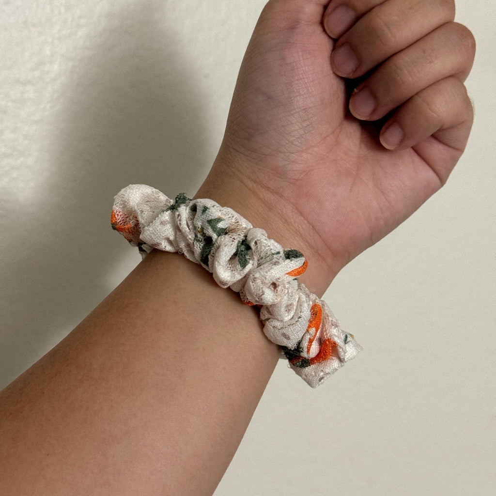 Hand wearing a floral scrunchie on a plain background